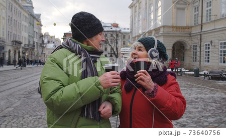 Senior old tourists grandmother grandfather walking, drinking hot drink mulled wine in city center Senior old tourists grandmother grandfather walking, drinking hot drink mulled wine in city center 73640756