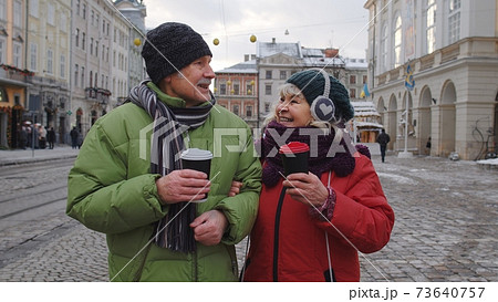 Senior wife husband tourists drinking from cups, enjoying hot drink tea on city central street Senior wife husband tourists drinking from cups, enjoying hot drink tea on city central street 73640757