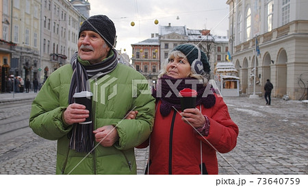 Senior wife husband tourists drinking from cups, enjoying hot drink tea on city central street Senior wife husband tourists drinking from cups, enjoying hot drink tea on city central street 73640759