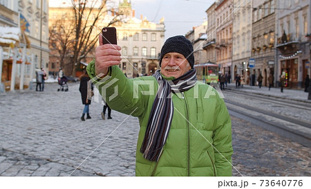 Senior man grandfather tourists traveling walking taking selfie pictures in European winter city Senior man grandfather tourists traveling walking taking selfie pictures in European winter city 73640776