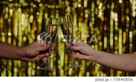 Two hands with glasses of champagne wine or cocktail making cheers, raising toast on gold background 73640856