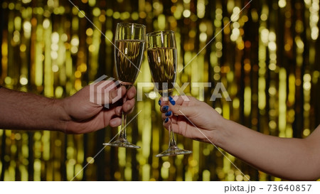 Two hands with glasses of champagne wine or cocktail making cheers, raising toast on gold background 73640857