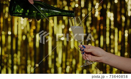 Champagne alcoholic drink is poured from bottle into drinking glasson gold background in slow motion Champagne alcoholic drink is poured from bottle into drinking glasson gold background in slow motion 73640858
