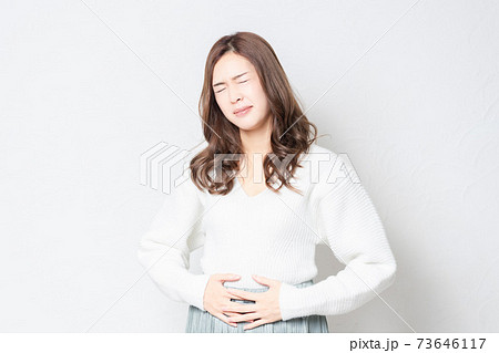 白い壁の前に立って、お腹に手を当てる若い女性 73646117