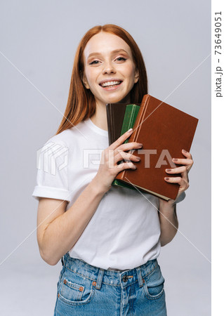 Cheerful young woman college student holding book and looking at camera on isolated background.  73649051