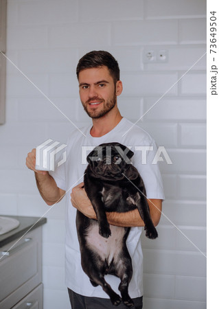 A man holds a pug dog in his arms, and drinks coffee A man holds a pug dog in his arms, and drinks coffee 73649504