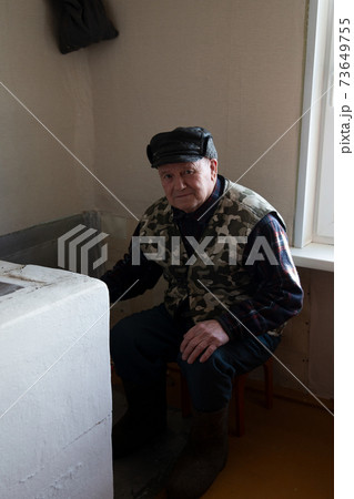 An old man puts wood in a heating stove in a country house in Russia, winter, Siberia An old man puts wood in a heating stove in a country house in Russia, winter, Siberia 73649755