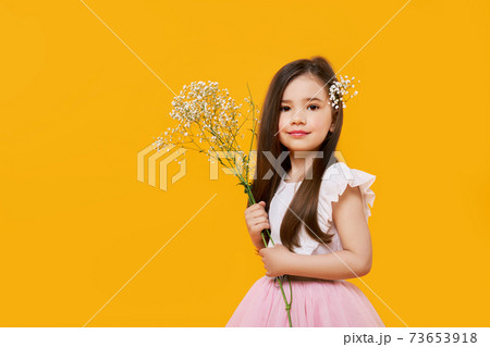 Cute young girl with wildflowers bouquet in hands on yellow background 73653918