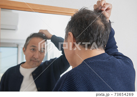 薄毛・抜け毛に悩む中高年男性　鏡を見て白髪を気にするシニア男性 73654269