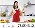 Happy Asian woman chef in red apron holding bowl of sunflower sprout in kitchen. 73654312
