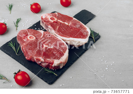 Raw rib-eye beef steak on wooden cutting board on gray background 73657771