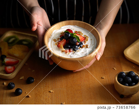 Female hands holding a bowl of granola with natural Greek yogurt and fresh berries 73658766