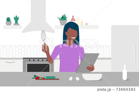 A young black woman looks on tablet and cooking by online video tutorial in her kitchen. Online culinary school. Online courses, e-learning. Eps 10 73660383