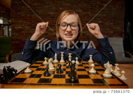 Little boy in eyeglasses sitting at home and playing chess alone. 73661370