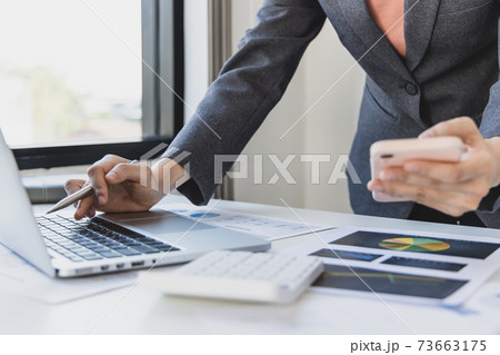 Finance workers are reviewing the company's financial data on a laptop and using smartphones to communicate or chat with the team at social distances, Working during the virus outbreak. 73663175