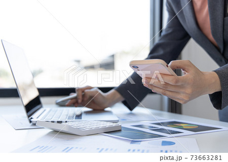 Finance workers are reviewing the company's financial data on a laptop and using smartphones to communicate or chat with the team at social distances, Working during the virus outbreak. 73663281