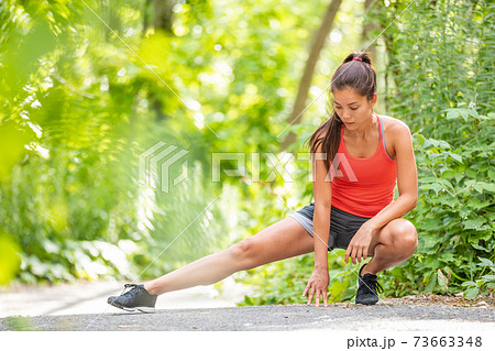 Runner woman stretching leg running workout run girl doing legs stretches outdoor in summer park. Asian athlete warm up prep before training. 73663348