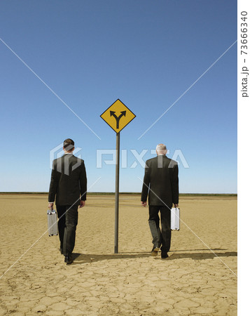 Businessmen Walking Past Road Sign In Desert Businessmen Walking Past Road Sign In Desert 73666340