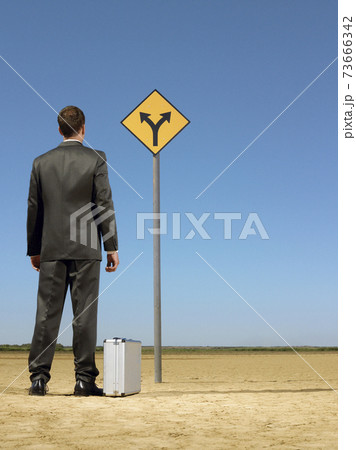 Businessman Looking At Road Sign On Desert Businessman Looking At Road Sign On Desert 73666342