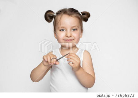 A little girl with blonde hair in two ponytails, posing to camera with happy smile on isolated studio white background, while making manicure procedure using scissors A little girl with blonde hair in two ponytails, posing to camera with happy smile on isolated studio white background, while making manicure procedure using scissors 73666872