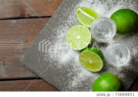 Tequila silver shots with lime slices and salt on wooden board Tequila silver shots with lime slices and salt on wooden board 73669851