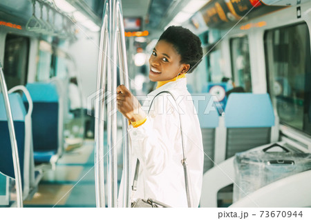 A smiling young African woman holds on to a handrail while standing on a subway train during her daily commute to work 73670944