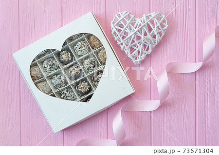 Chocolate handmade candies on pink wooden table. Chocolate box with heart and a festive ribbon. Gift for valentine's day Chocolate handmade candies on pink wooden table. Chocolate box with heart and a festive ribbon. Gift for valentine's day 73671304