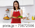 Asian woman chef in red apron holding salmon steak, serving on wooden board. Concept woman preparing meals at home. 73672506