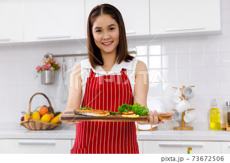 Asian woman chef in red apron holding salmon steak, serving on wooden board. Concept woman preparing meals at home. Asian woman chef in red apron holding salmon steak, serving on wooden board. Concept woman preparing meals at home. 73672506