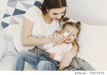 Mother with thermometer is sitting near daughter Mother with thermometer is sitting near daughter 73672970