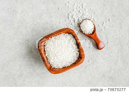 Salt in wooden bowl with scoop on gray stone table. Sea salt flat lay, top view.  73673277