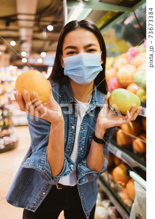Cheerful young woman in protective mask buys oranges Cheerful young woman in protective mask buys oranges 73673384