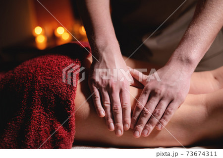 Male masseur doing massage of the knee to a woman patient in a dark room of a spa salon Male masseur doing massage of the knee to a woman patient in a dark room of a spa salon 73674311