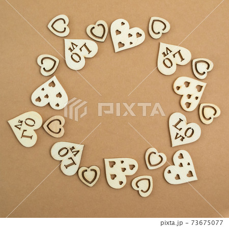 Wooden hearts on a pastel craft paper background in the form of a round frame. Abstract background with wood cut shapes. Sainte Valentine. Copy space. Wooden hearts on a pastel craft paper background in the form of a round frame. Abstract background with wood cut shapes. Sainte Valentine. Copy space. 73675077