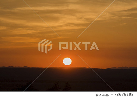 オレンジ色の空とシルエットになった大地と沈む太陽の風景の写真素材
