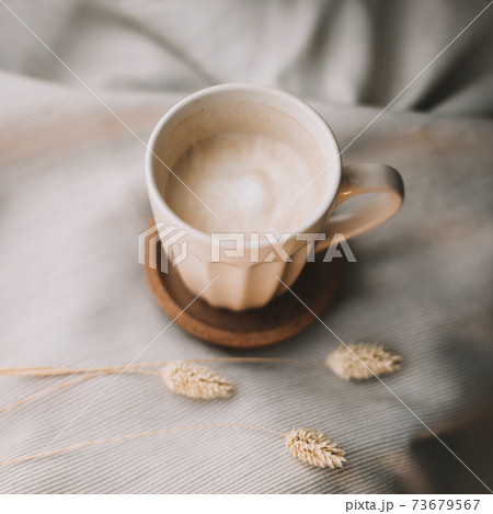 Cup of coffee with milk on beige plaid. Flat lay, top view still life morning breakfast. Comfort, cosiness and warmth concept. Photo in light pastel colors Cup of coffee with milk on beige plaid. Flat lay, top view still life morning breakfast. Comfort, cosiness and warmth concept. Photo in light pastel colors 73679567