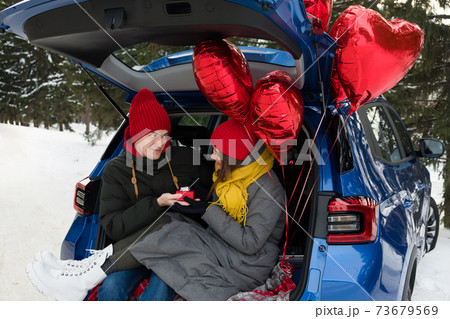 Valentine Gift. Happy Young Couple with Valentine's Day or birthday present. Happy Man giving a gift to his Girlfriend. Love concept. Couple sitting in car trunk 73679569