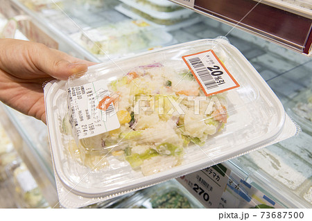 割引シールの貼ってあるお惣菜を手に取る女性買い物客手元 73687500