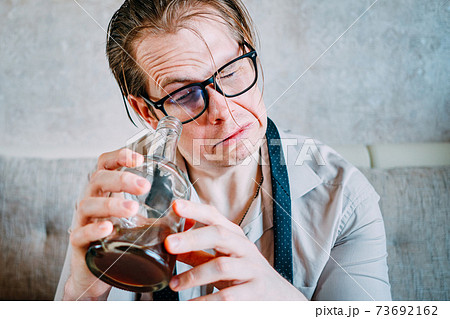 A drunk man drinks alcohol from a bottle. 73692162
