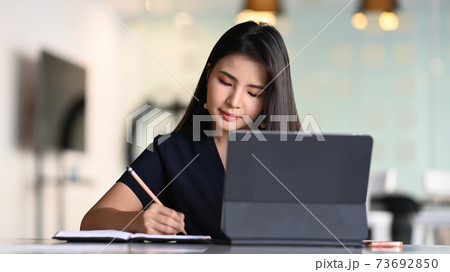 Businesswoman working with tablet computer and concentrate writing in formation on notebook. Businesswoman working with tablet computer and concentrate writing in formation on notebook. 73692850
