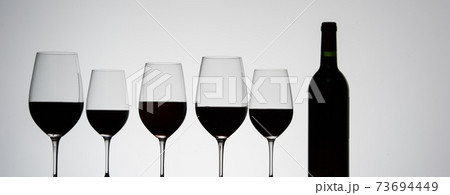 Glasses with red grape wine and bottle on a white glossy surface Glasses with red grape wine and bottle on a white glossy surface 73694449