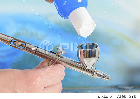 Artist fills the airbrush canister with blue paint 73694539