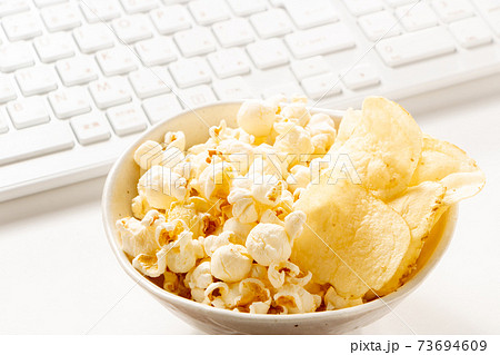オンライン飲み会のおつまみイメージ。ポップコーンとポテトチップスの盛り合わせとキーボード。 73694609