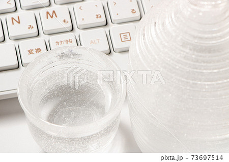 日本酒の入ったガラス製の酒器と、パソコンのキーボード。オンライン飲み会イメージ。 73697514