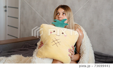 Young woman sitting on sofa and thinking. Beautiful girl holding cushion Young woman sitting on sofa and thinking. Beautiful girl holding cushion 73699441