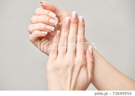 Beautiful Female Hands with French manicure over light grey background Beautiful Female Hands with French manicure over light grey background 73699950