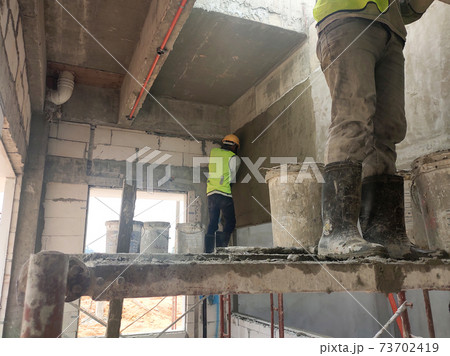 IPOH, MALAYSIA -MAY 25, 2020: Plastering work by construction workers using the cement plaster. Scaffolding used as temporary staging to work at height. Wearing appropriate safety gear to prevent an a 73702419