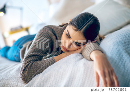 Dark-haired woman lying on bed and looking depressed Dark-haired woman lying on bed and looking depressed 73702891