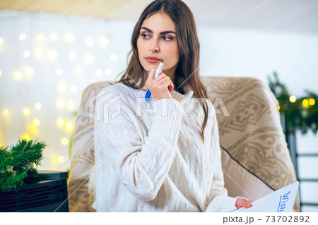 Young woman writing something and looking thoughtful Young woman writing something and looking thoughtful 73702892
