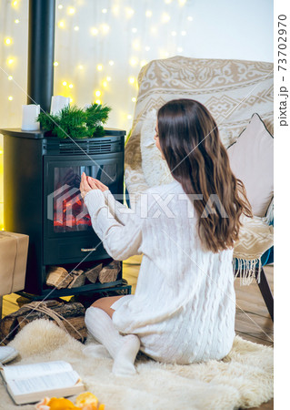 Young woman in white clothes and stockings sitting near the fireplace 73702970